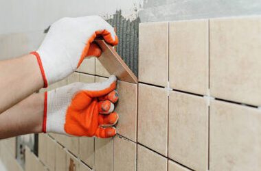 tegel3 Worker sets tiles on the wall in the kitchen. His hands are placing the tile on the adhesive.